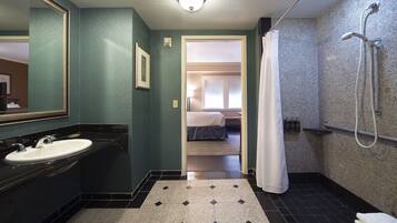 A bathroom with a sink, mirror, shower, and a door leading to a bedroom.