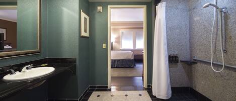 A bathroom with a sink, mirror, shower, and a door leading to a bedroom.