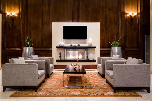 A modern living room with a fireplace, a flat-screen TV, and grey sofas arranged around a coffee table. - The Whitehall Houston (Houston)