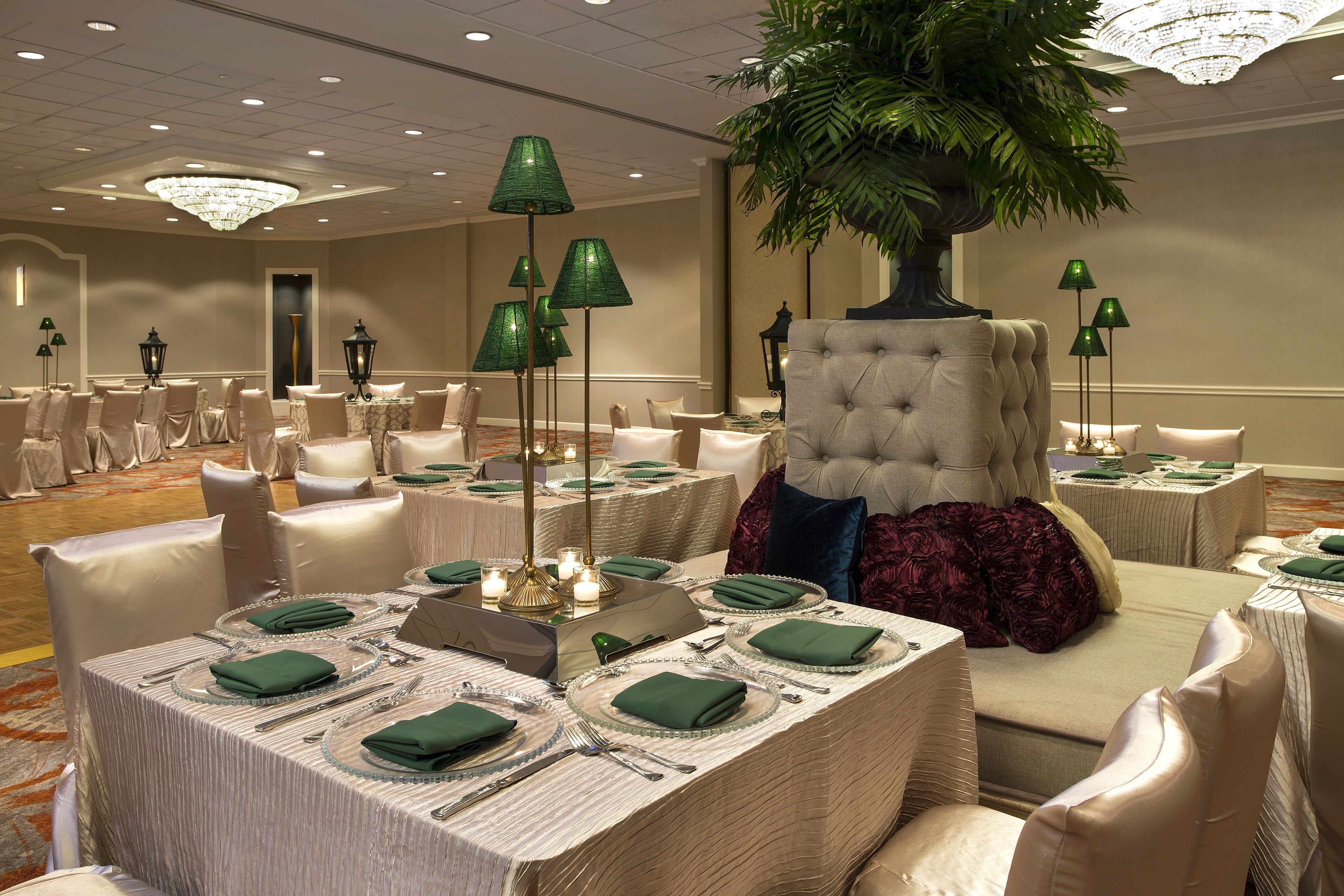 A banquet hall with round tables, green tablecloths, and white chairs.