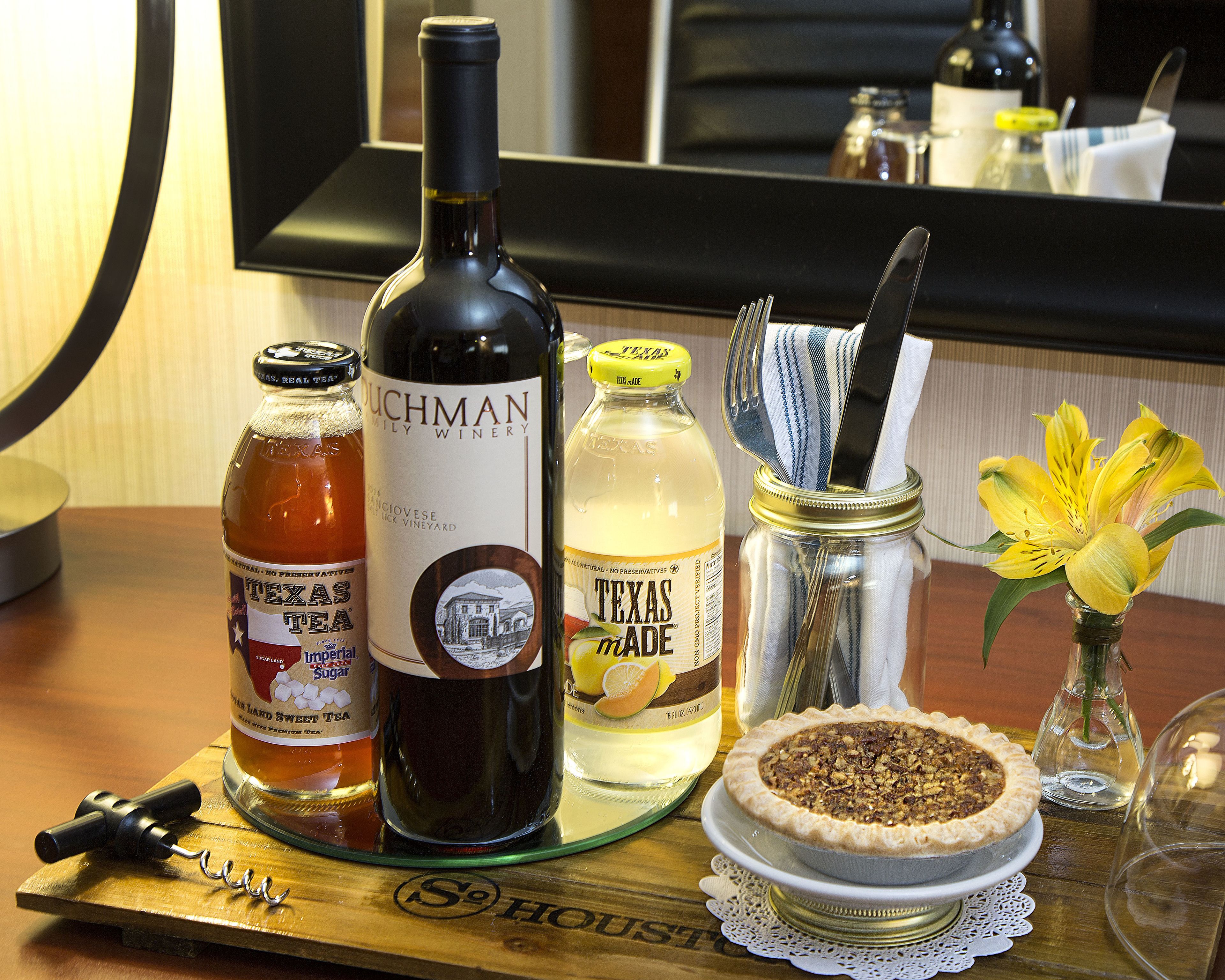 Ein Holztisch mit einer Flasche Texas Sweet Tea, einer Flasche Texas Made, einem Einmachglas mit Stofftuch und einem Kuchen auf einer Glasschale.
