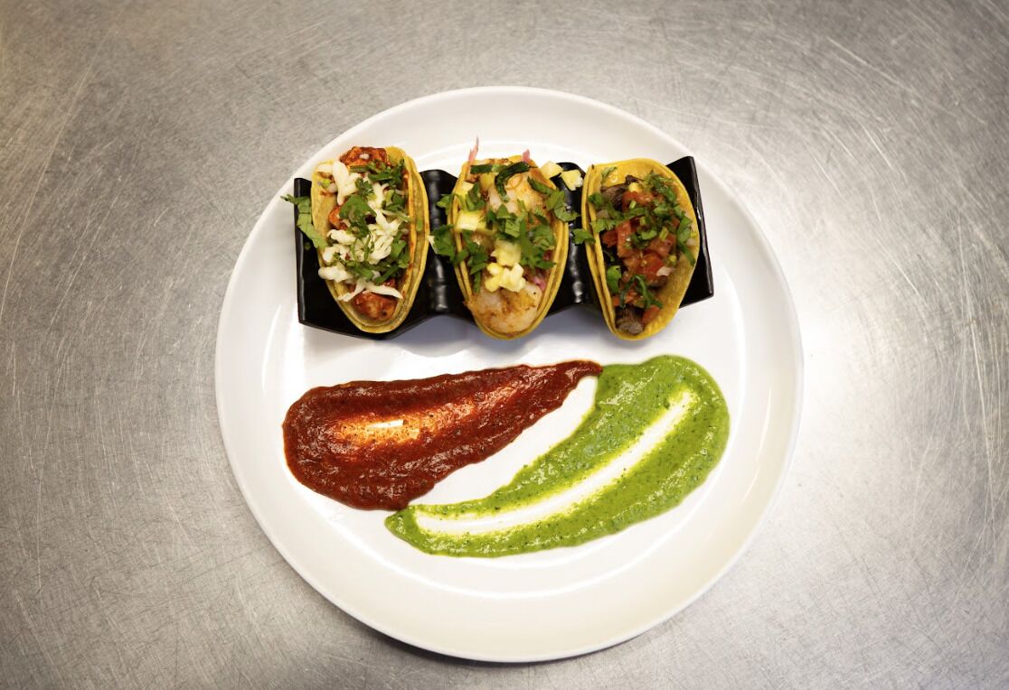A plate with three tacos and two sauces.