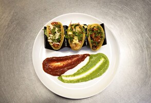 A plate with three tacos and two sauces.