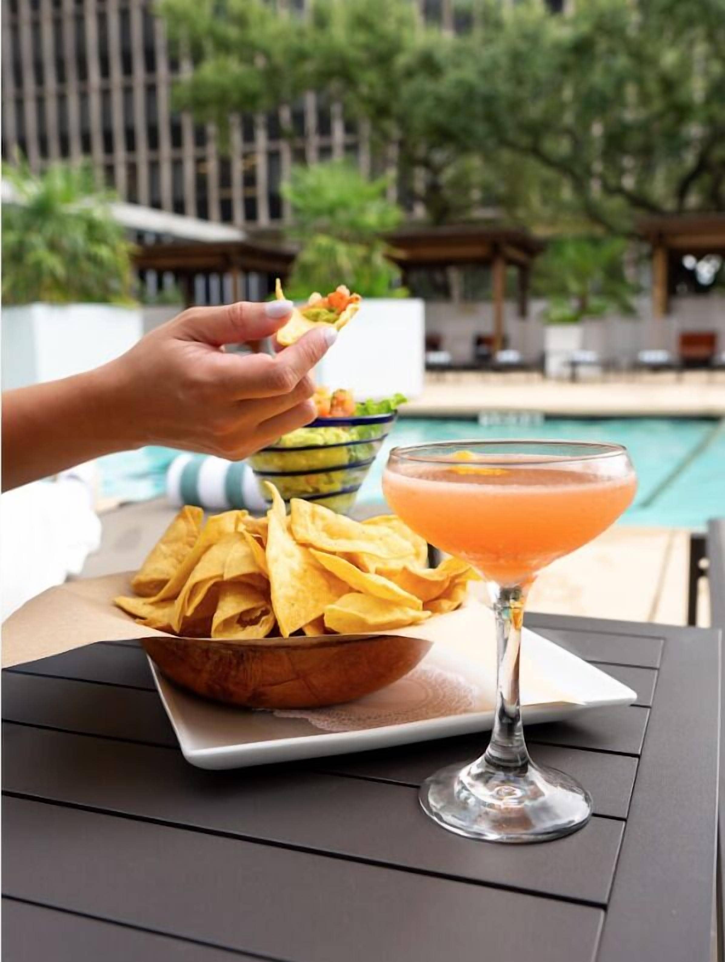 A dining table with a bowl of chips, a martini glass, and a pool in the background.