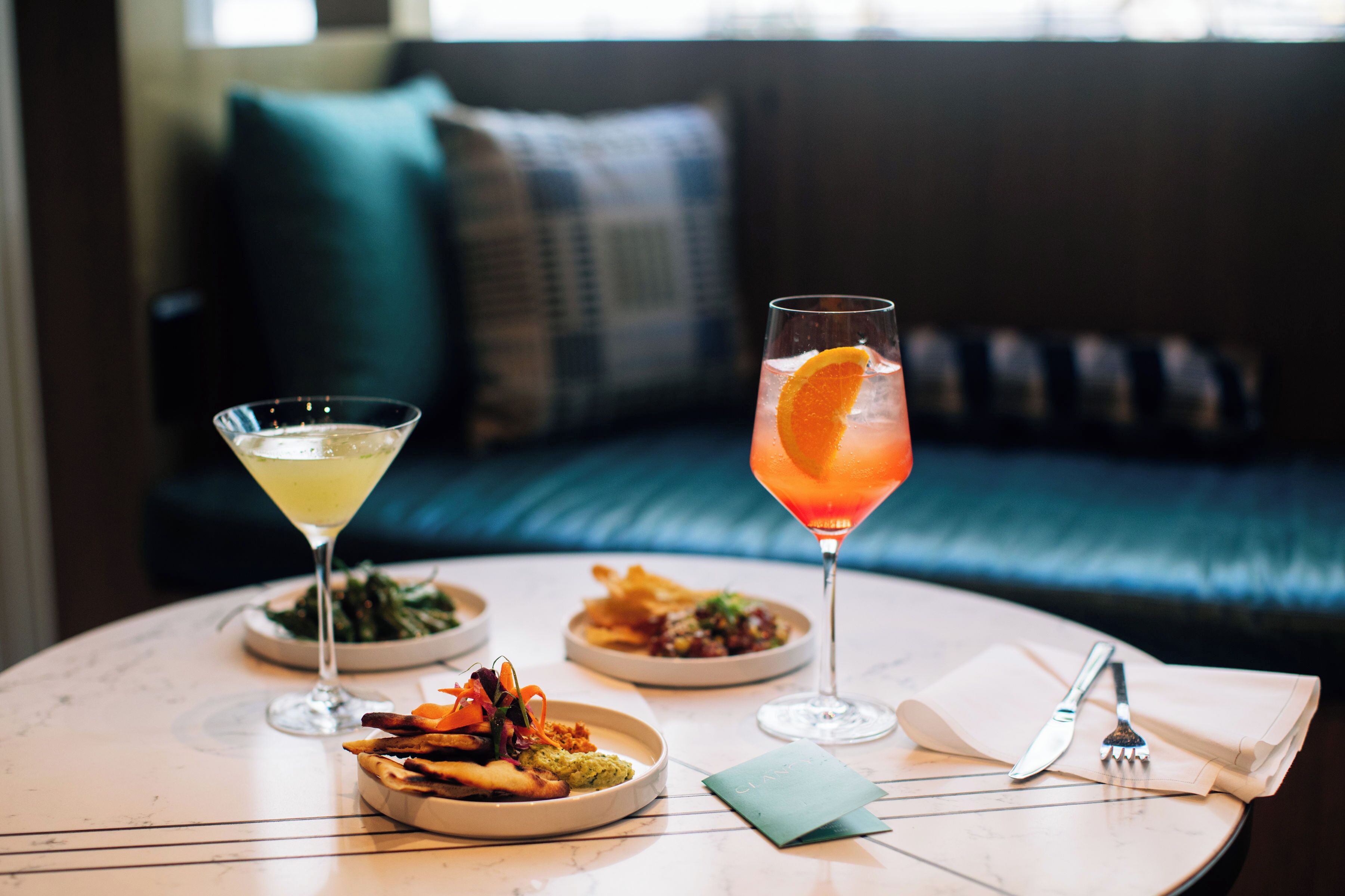 Una mesa redonda con dos copas de martini, un plato de comida y un guardanapo con cubiertos.