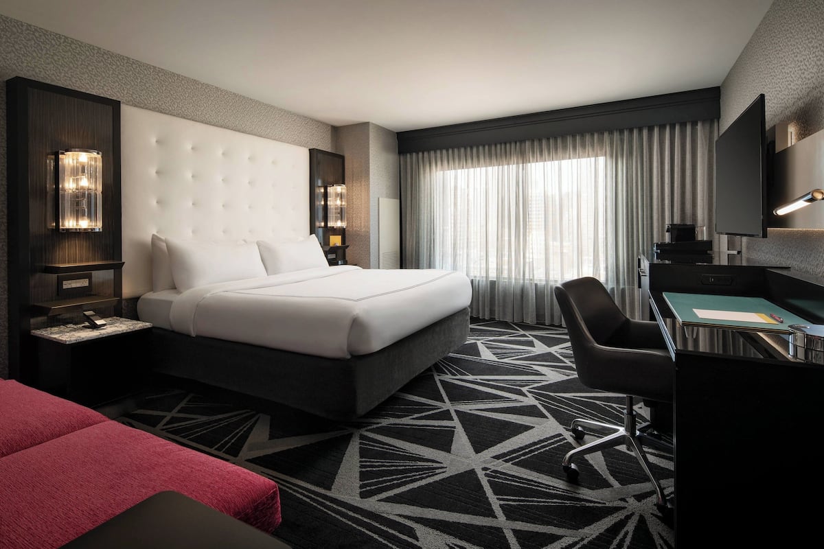 A hotel room with a large bed, a desk, a chair, and a TV.