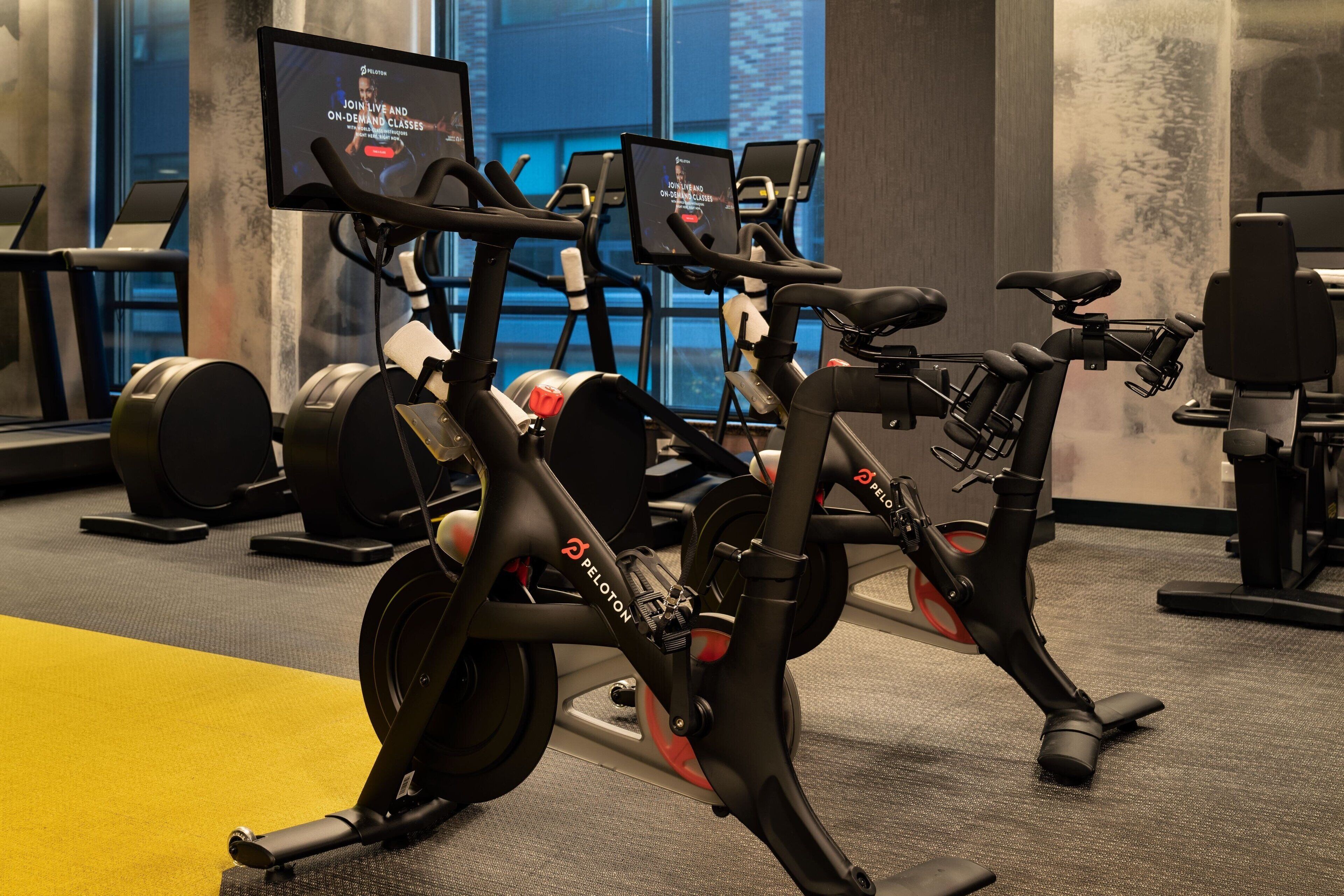 A Peloton exercise bike in a gym with a large window in the background.