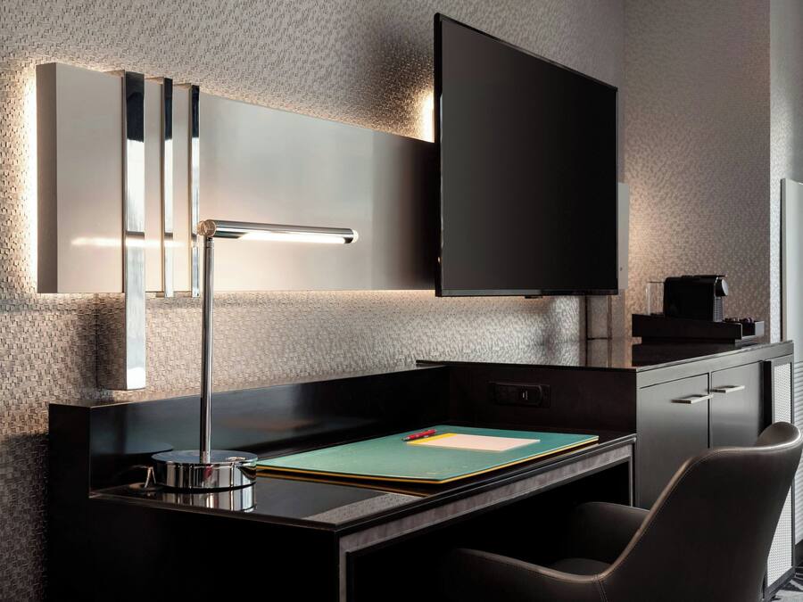 Una habitación de hotel moderna con un escritorio elegante, un televisor de pantalla plana montado en la pared y un espejo grande sobre el escritorio.