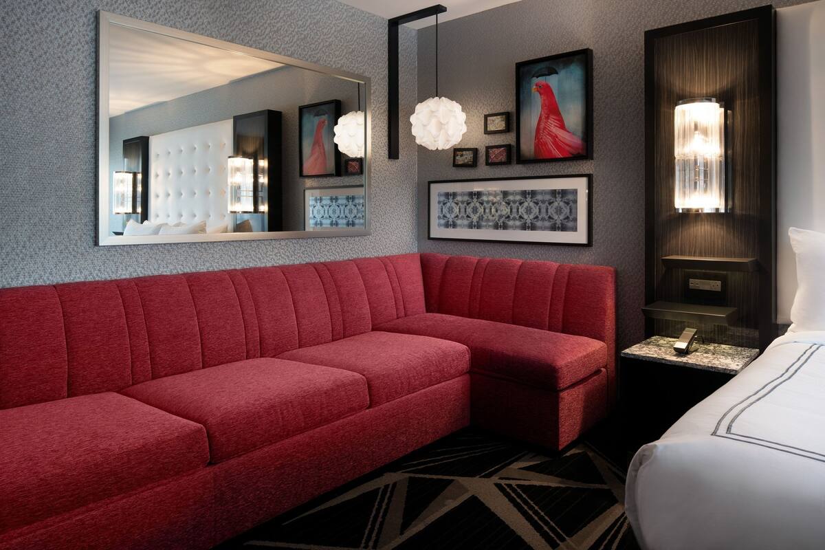 A modern hotel room with a red sofa, a large mirror, and artwork on the walls.