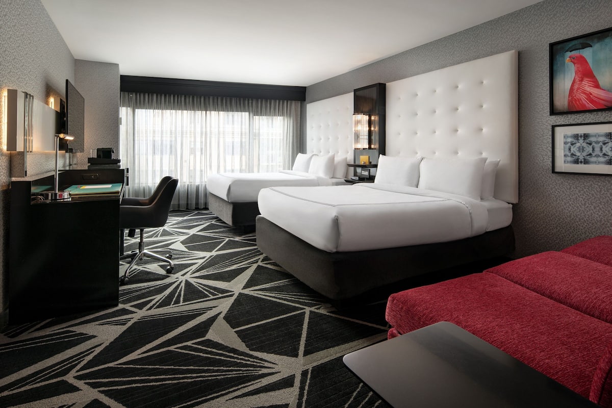A hotel room with two beds, a desk, and a large window with curtains.