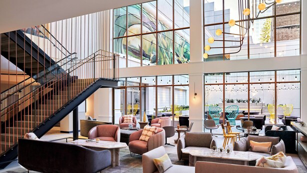A spacious lobby with a staircase, comfortable seating areas, and large windows offering views of the city. -  The Clancy, Autograph Collection by Marriott (San Francisco)
