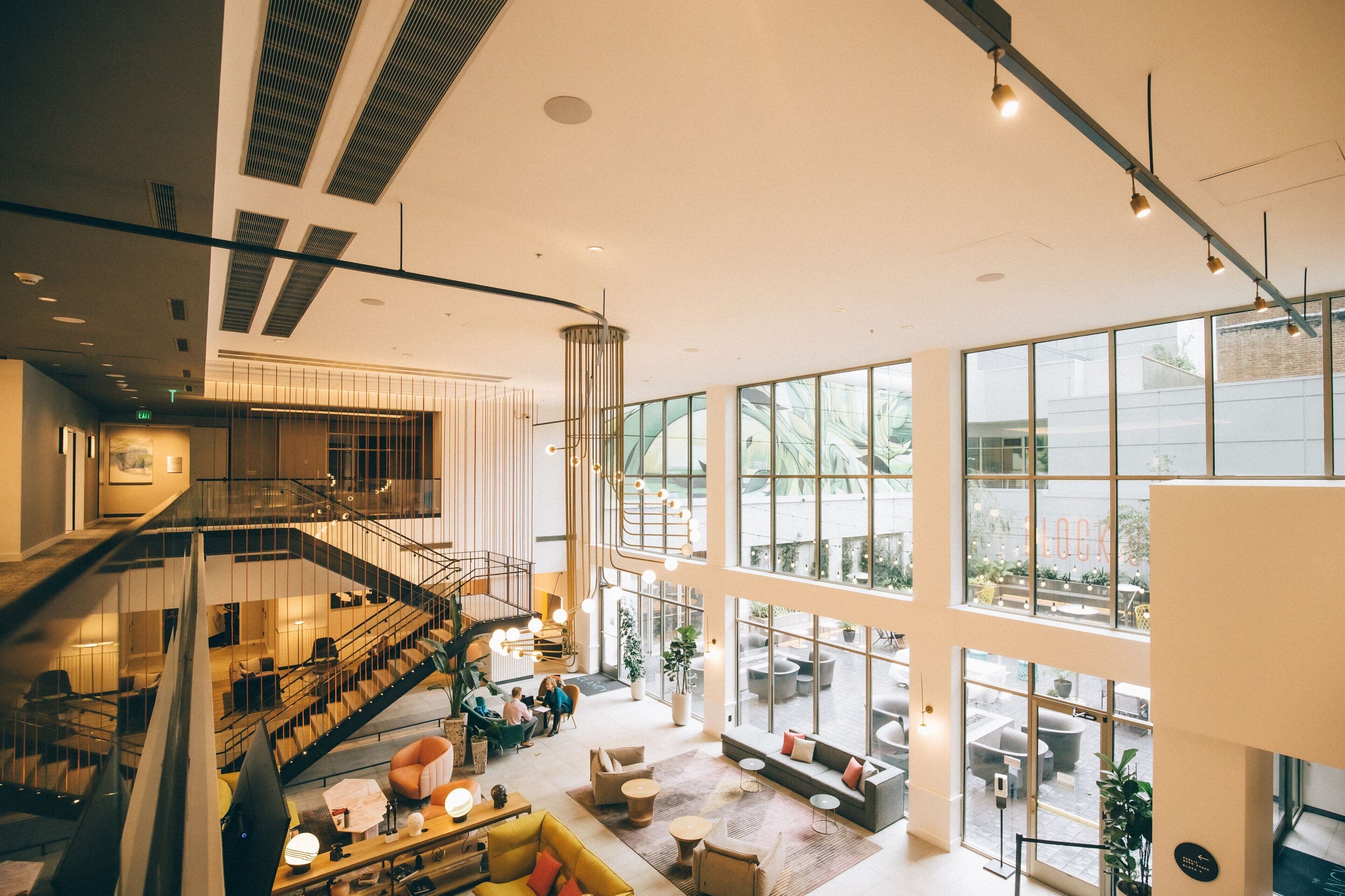 Eine geräumige Lobby mit hoher Decke, großen Fenstern, einer Treppe und Sitzbereichen.