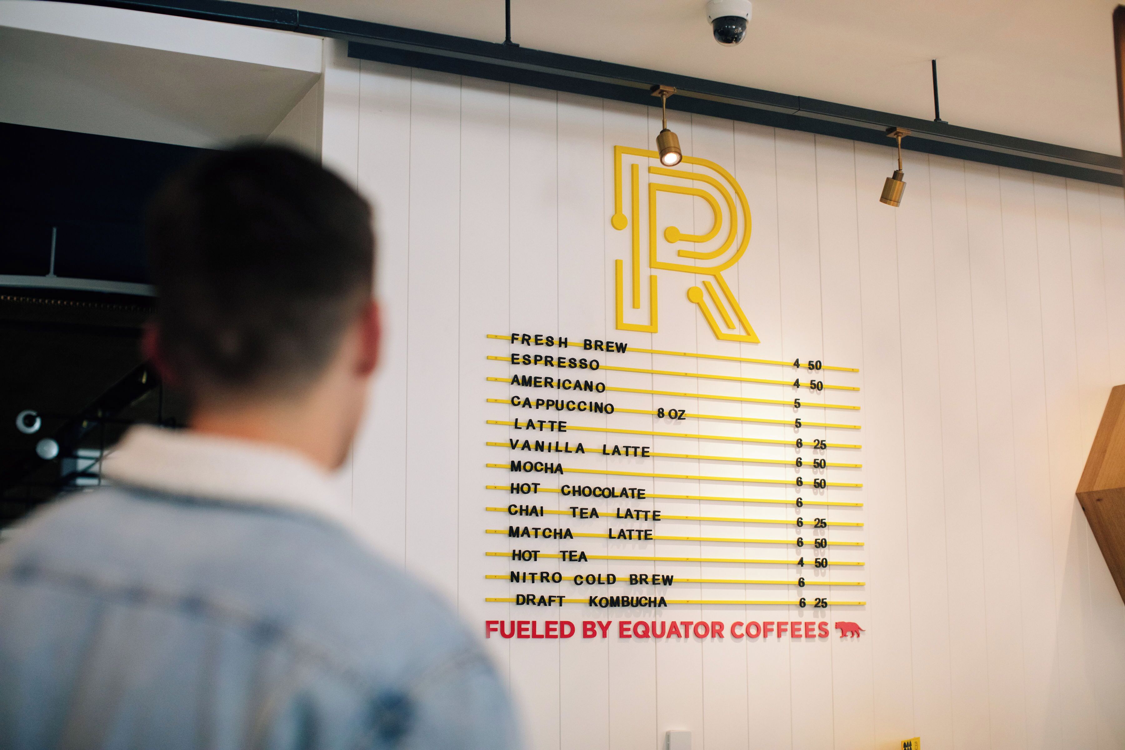 A menu board with coffee and drink options, a large 'R' logo, and a sign stating 'FUELED BY EQUATOR COFFEEES'.