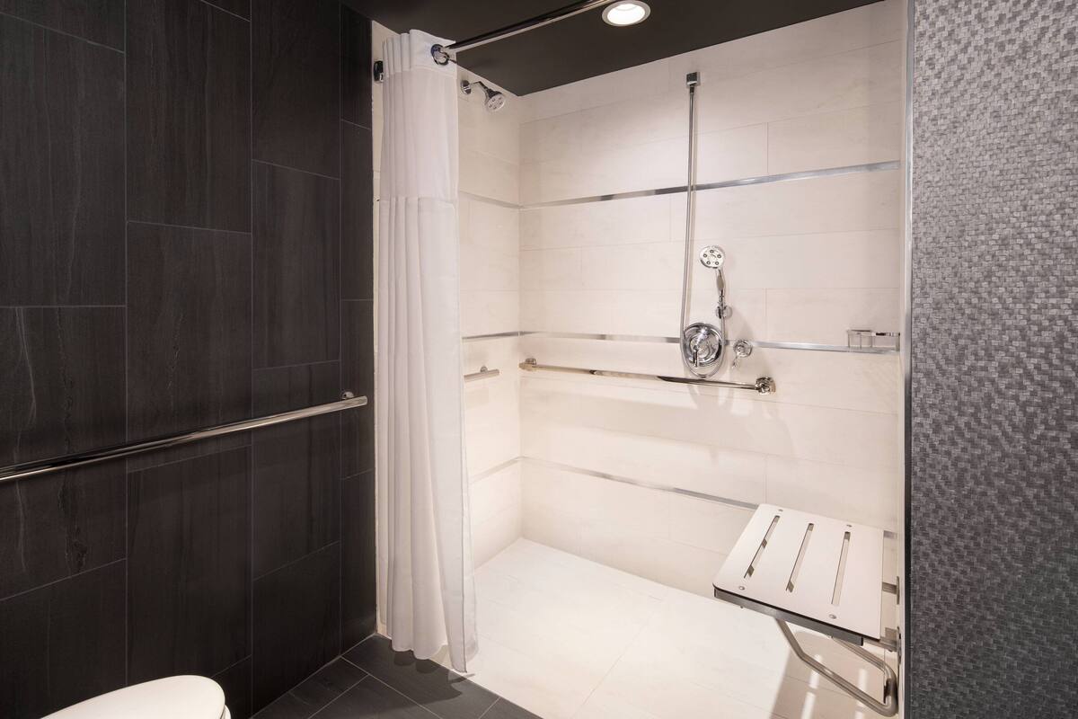 A modern bathroom with a glass-enclosed shower, dark tiled walls, and a white toilet.