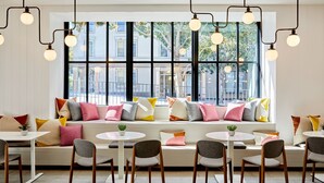 A modern cafe with a large window, white walls, and a variety of seating options including tables and a bench. -  The Clancy, Autograph Collection by Marriott (San Francisco)