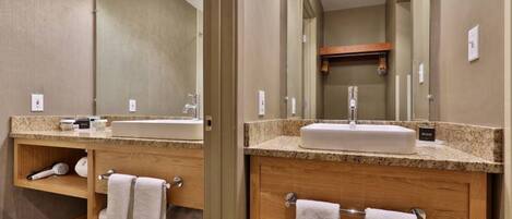 Un baño de hotel con encimera de granito, un lavabo, un espejo y un mueble de tocador de madera.