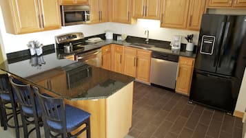 A kitchen with wooden cabinets, a black refrigerator, a stainless steel oven, and a granite countertop.