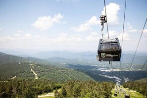 Eine Kabseilbahn mit dem Logo "Killington", die über eine gebirgige Landschaft mit dichten Wäldern und blauem Himmel schwebt.