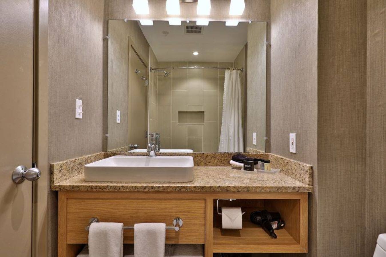 Un baño de hotel con lavamanos, espejo, ducha y toallero.