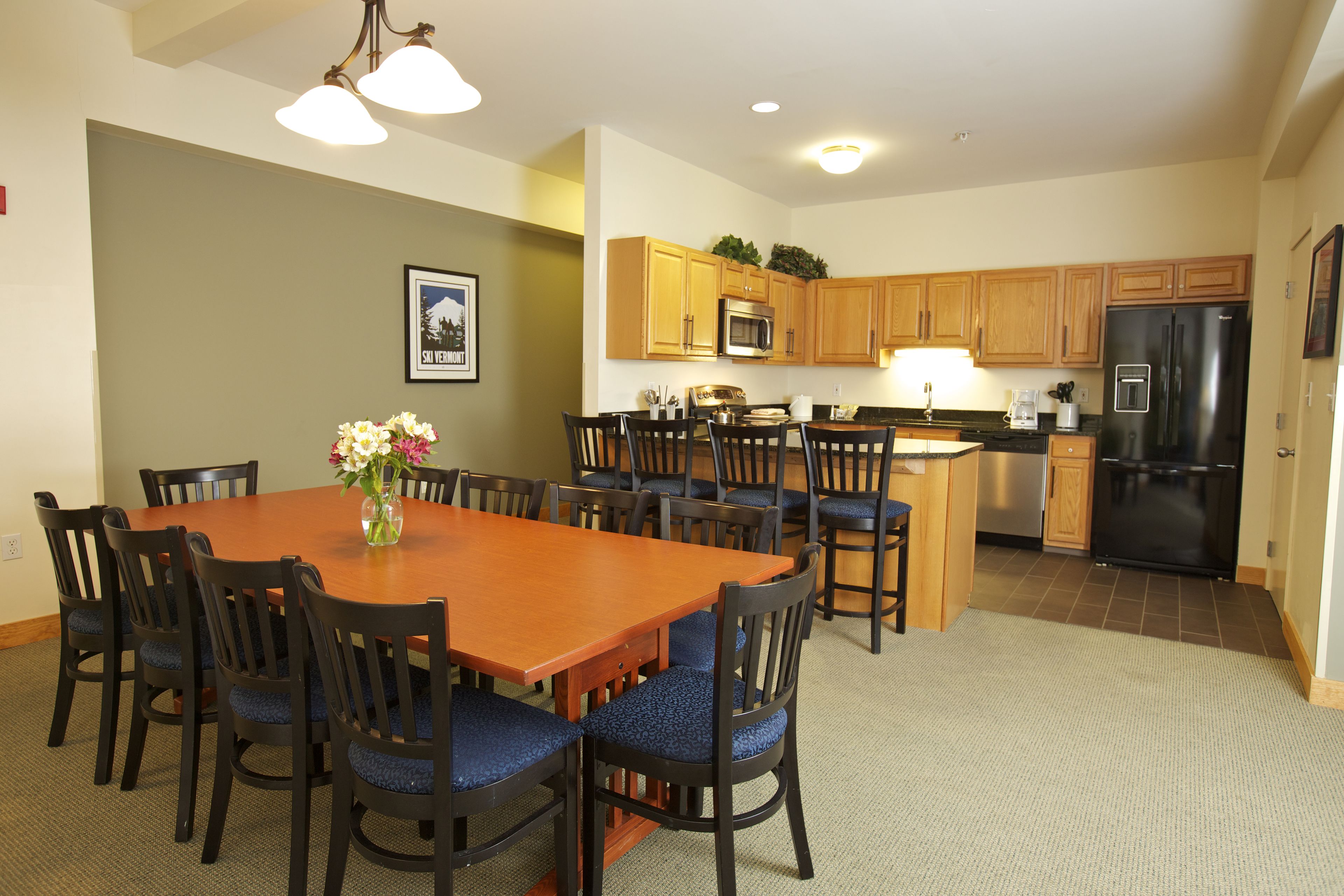 A dining area with a wooden table and chairs, a kitchen with wooden cabinets and appliances, and a framed picture on the wall.