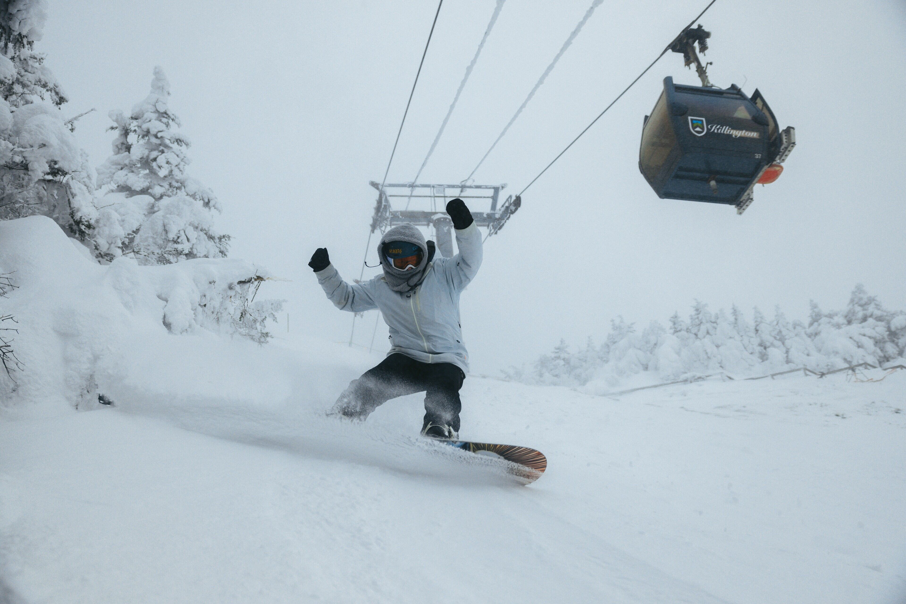 A person snowboarding down a snowy slope with a ski lift in the background.