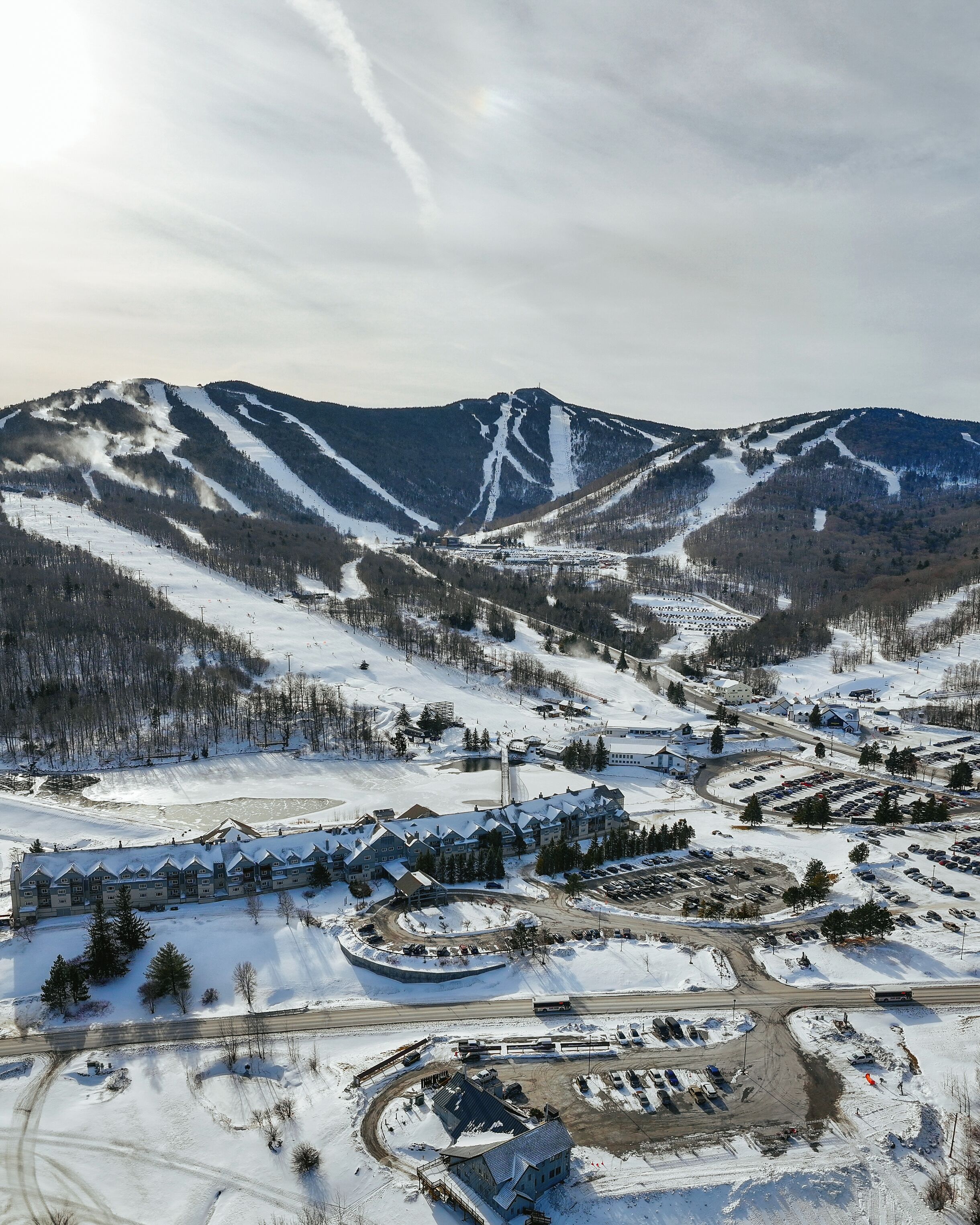 A snow-covered mountain resort with ski slopes, a parking area, and a lodge with multiple buildings.