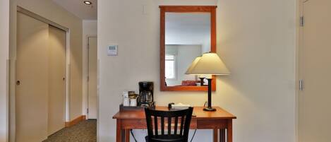 A hotel room with a wooden desk, a chair, a lamp, and a coffee maker.