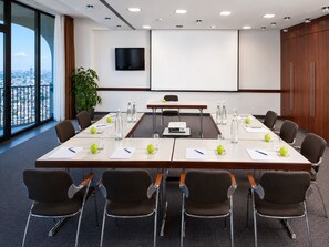 A conference room with a long table, chairs, a projector, and a large screen.
