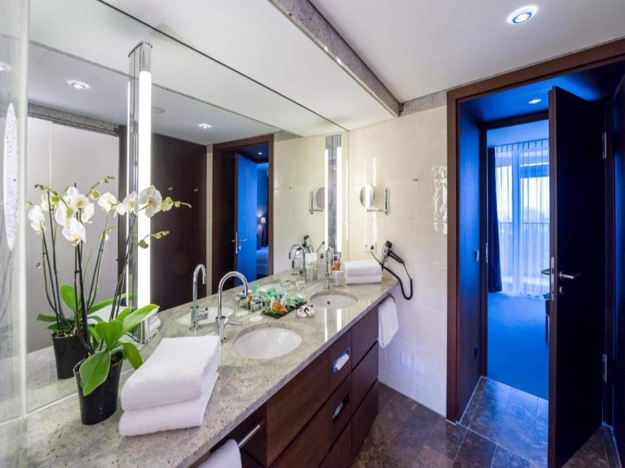 Un baño moderno con dos lavamanos, un espejo grande y una orquídea en maceta.