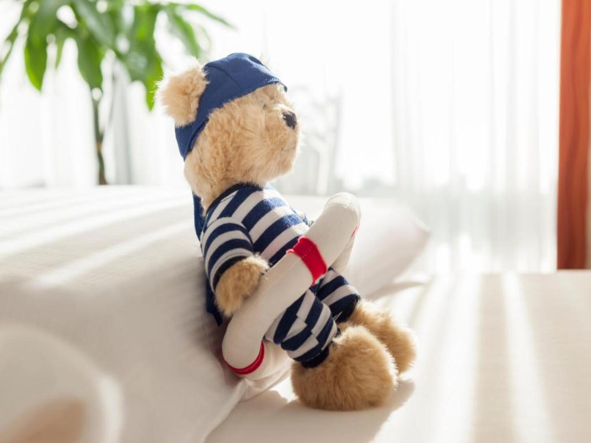 Un osito de peluche en una cama, vestido con un conjunto a rayas y un gorro azul.