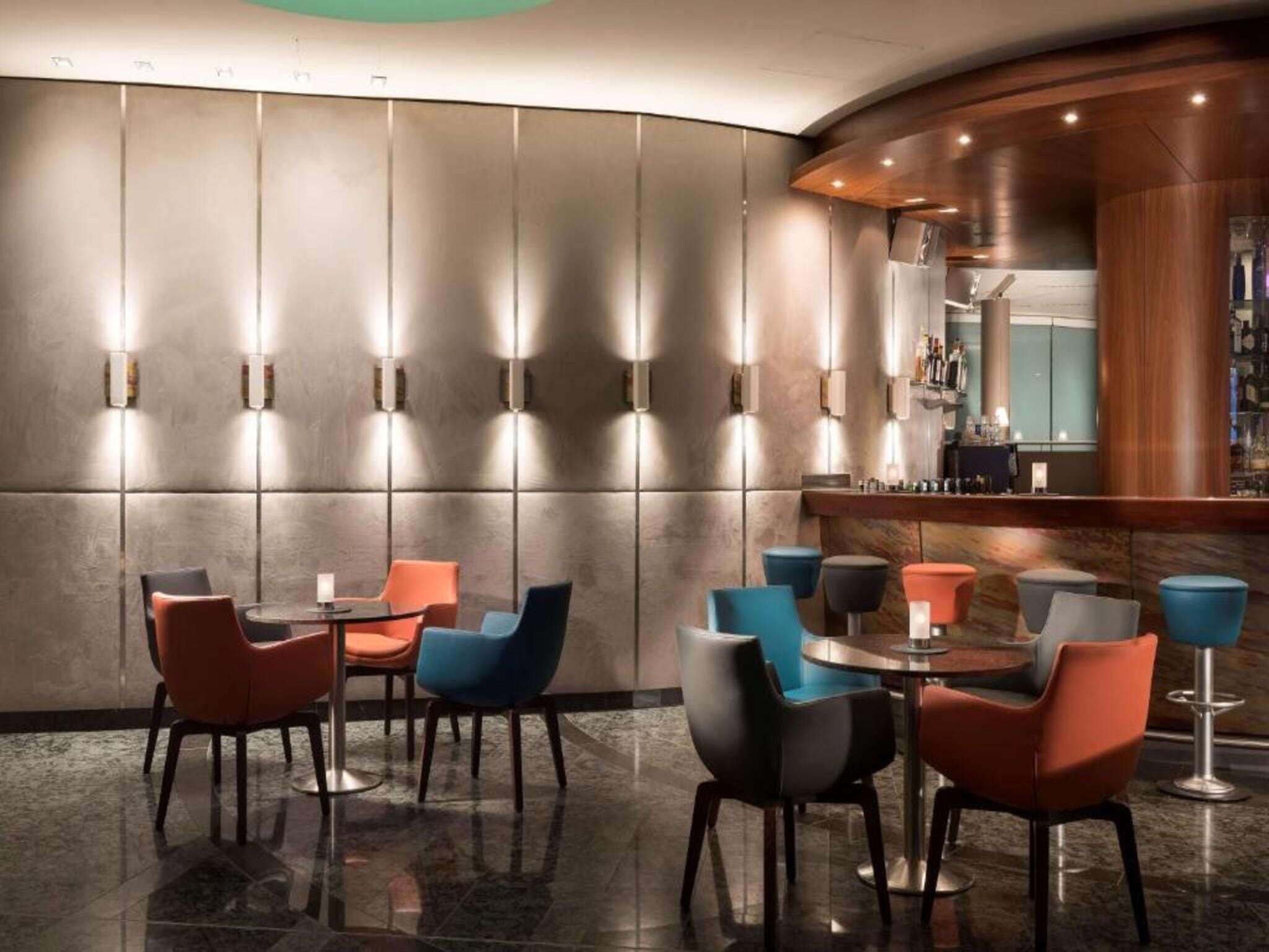 A modern bar area with round tables and chairs, a curved counter, and wall-mounted lighting.