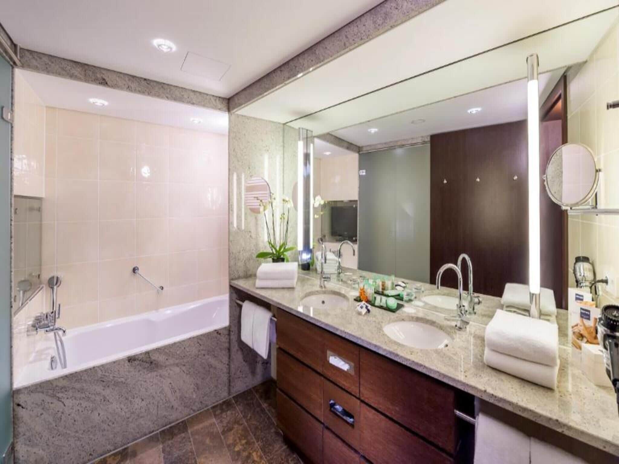 Un baño moderno con bañera, dos lavamanos, un espejo grande y un mueble de tocador con cajones.