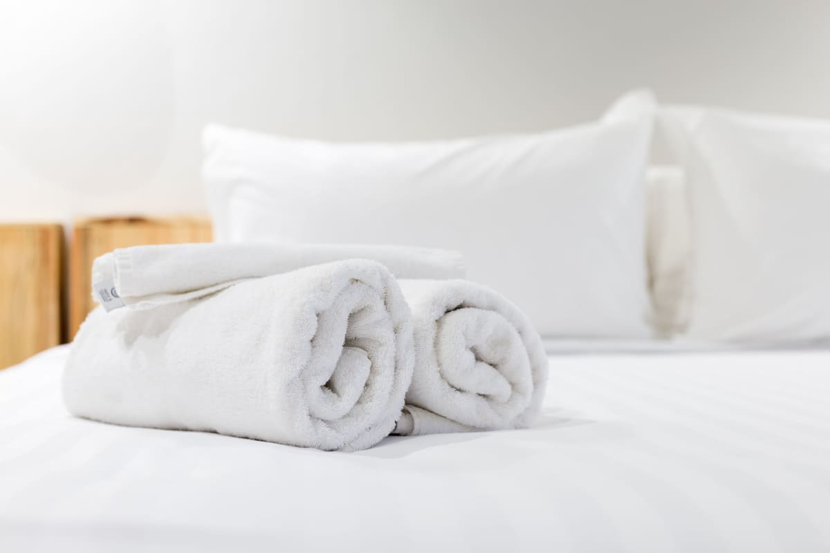 A neatly made bed with white linens and rolled towels.