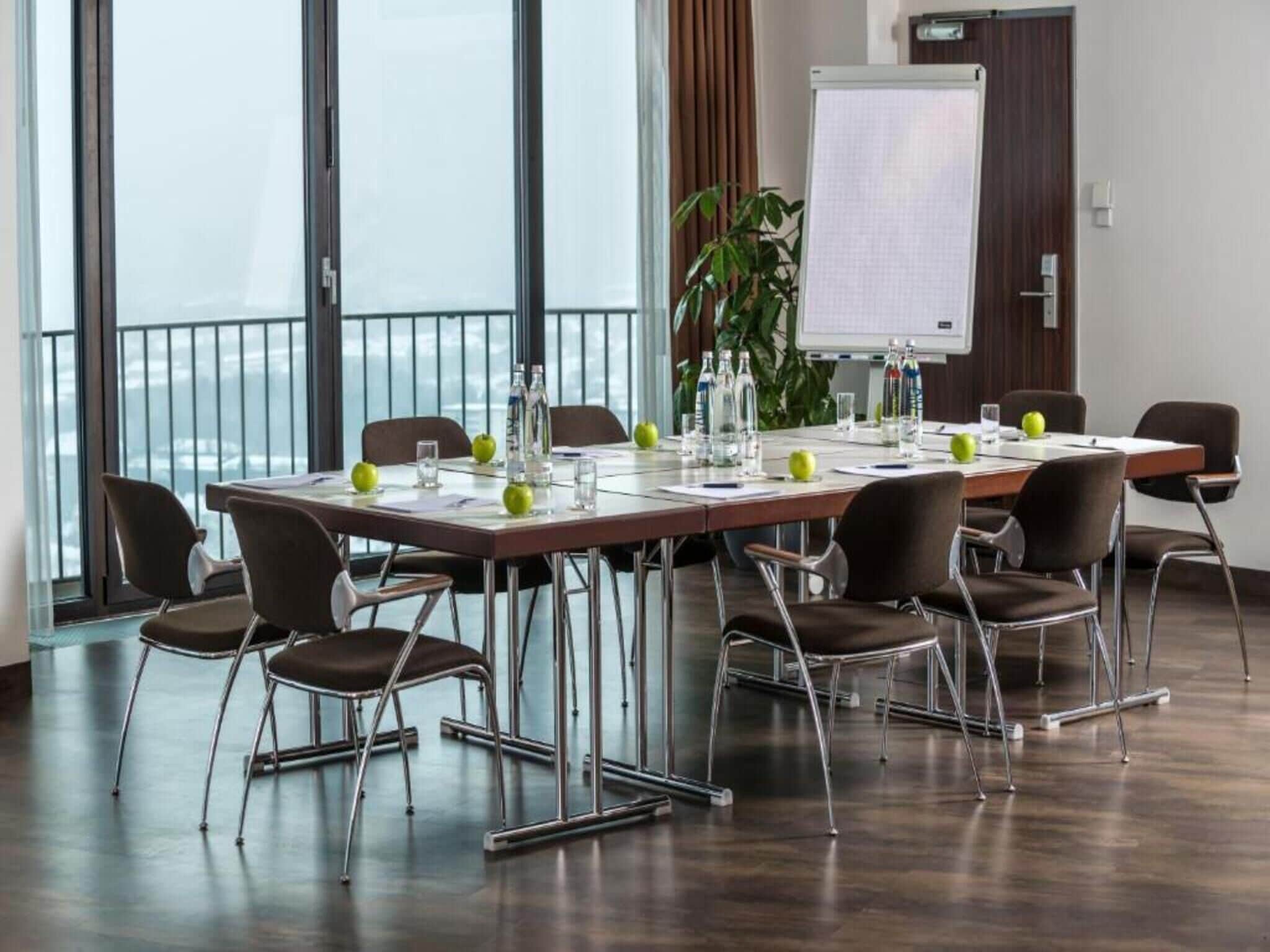 Un salón de conferencias con una gran mesa, sillas, una pizarra y una planta.