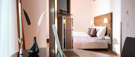 Een hotelkamer met een bed, een bureau met een laptop, een vaas en een lamp.