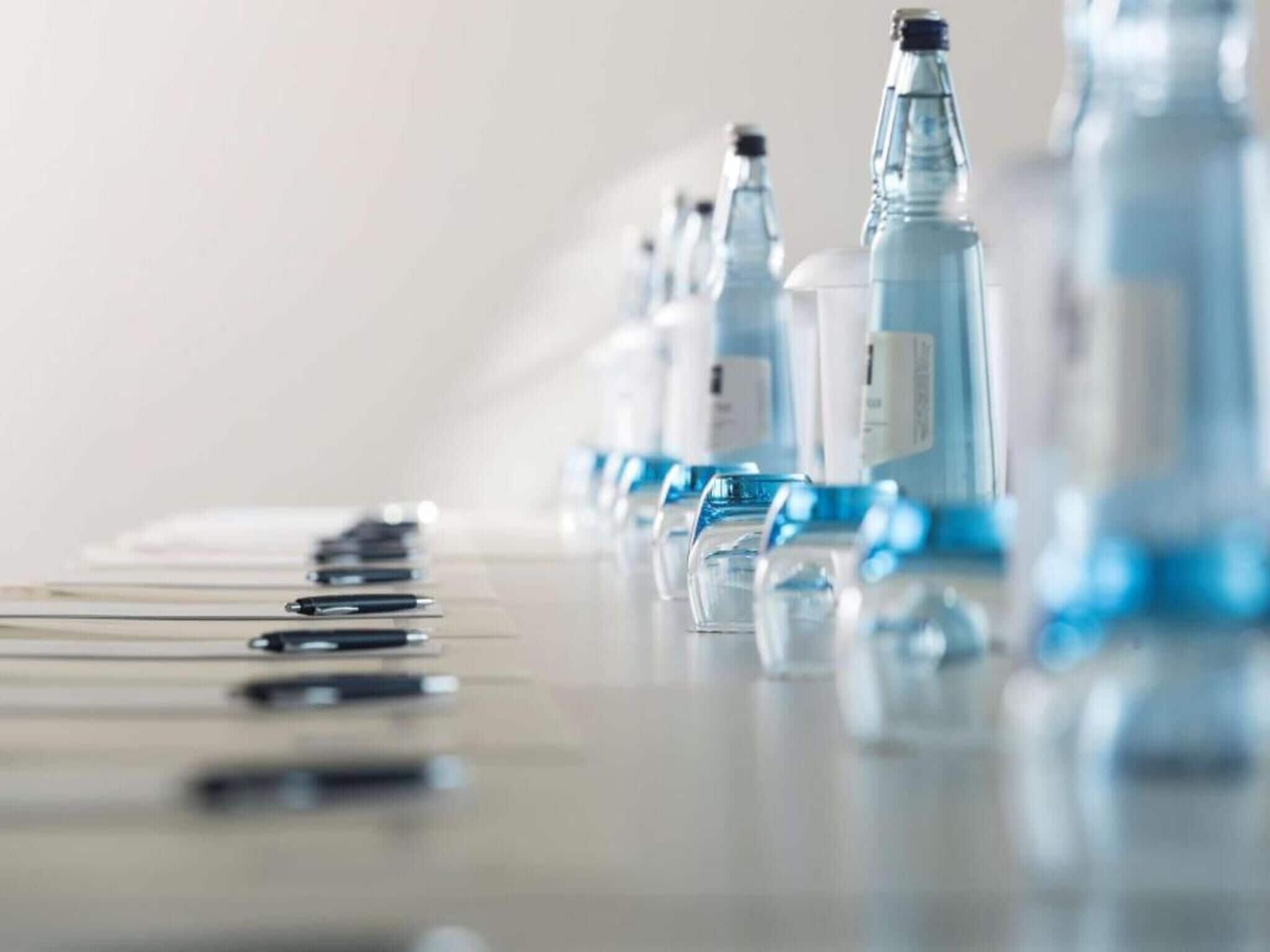 Une rangée de bouteilles en verre transparent, toutes munies d’étiquettes, disposées sur une surface réfléchissante.