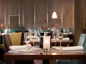 Un ambiente de restaurante con mesas dispuestas para comer, destacando copas de vino, una vela y un florero con flores.