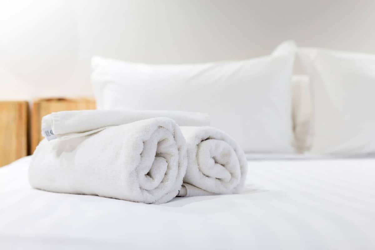 A neatly made bed with white linens and rolled towels.