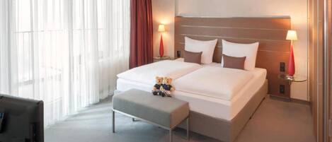 A hotel room with two beds, a desk, a chair, and a window with curtains.