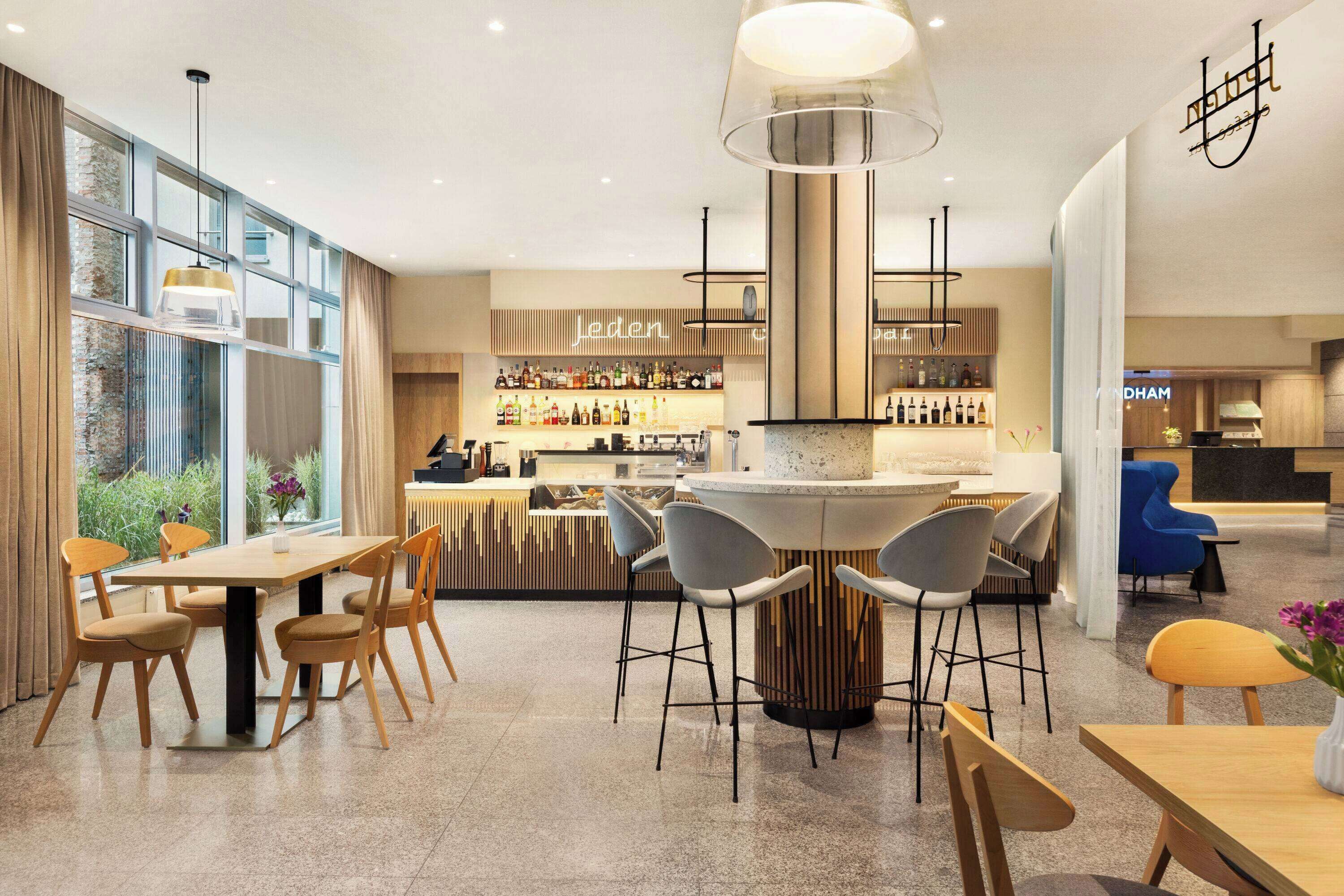 A modern bar area with a central bar counter, seating arrangements, and a large window providing natural light.
