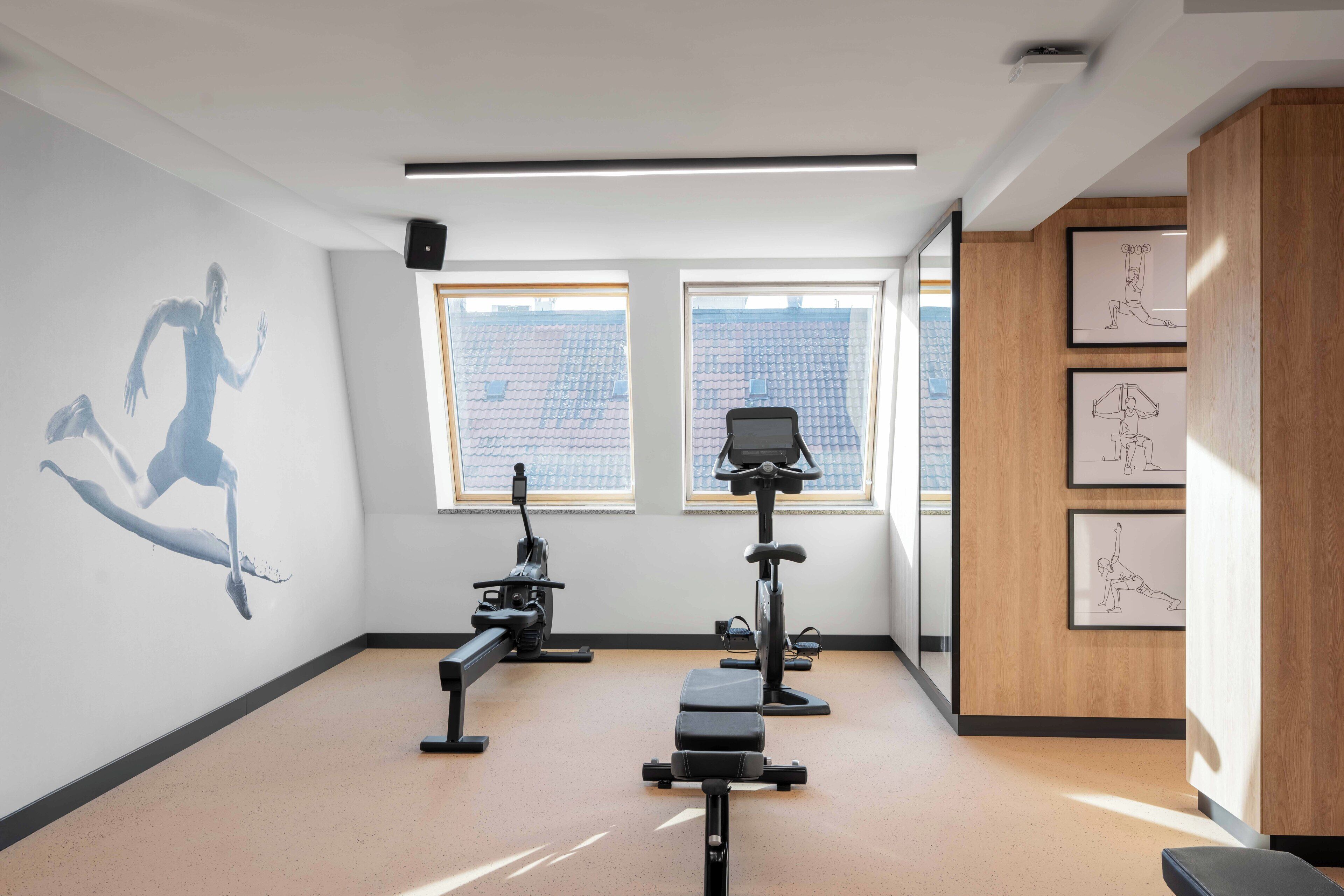 A gym with exercise equipment, large windows, and artwork on the walls.