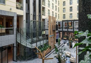 Un moderno vestíbulo de hotel con una escalera central, zonas de estar y una recepción.