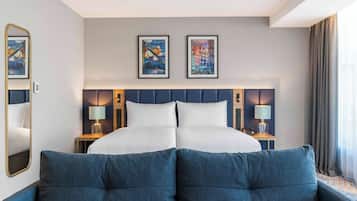 Habitació d'hotel amb un llit gran, dues taules de nit amb làmpades, un capçal de llit amb obra d'art i una finestra gran amb cortines.