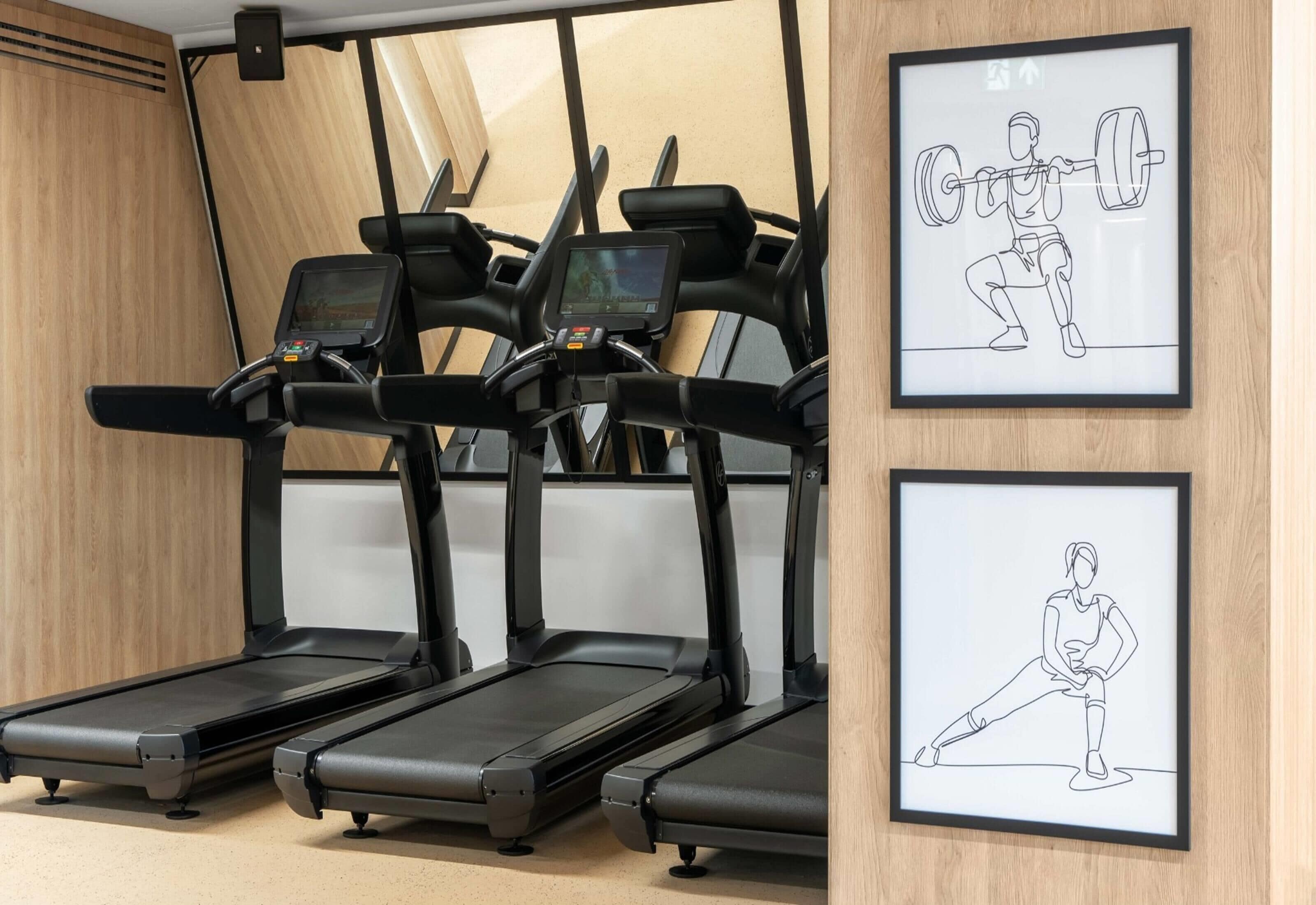 Three treadmills in a gym with wooden walls and framed exercise illustrations.