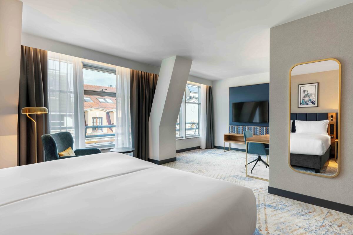 A hotel room with a large bed, a desk, a chair, a TV, and a window with curtains.