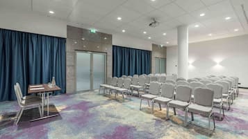 A conference room with rows of chairs, a projector, and a table with a glass.