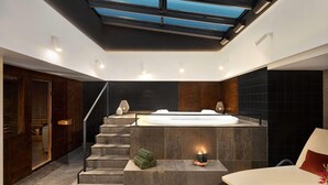 A modern spa area with a hot tub, a seating area, and a staircase leading to a wooden door. - Wyndham Wroclaw Old Town (Wroclaw)