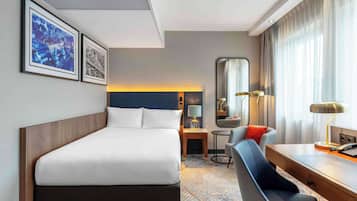 Ein Hotelzimmer mit einem Bett, einem Schreibtisch, einem Stuhl, einem Spiegel und zwei gerahmten Bildern an der Wand.