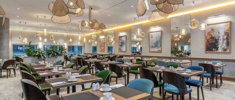 A spacious dining area with multiple tables and chairs, modern pendant lighting, and artwork on the walls.