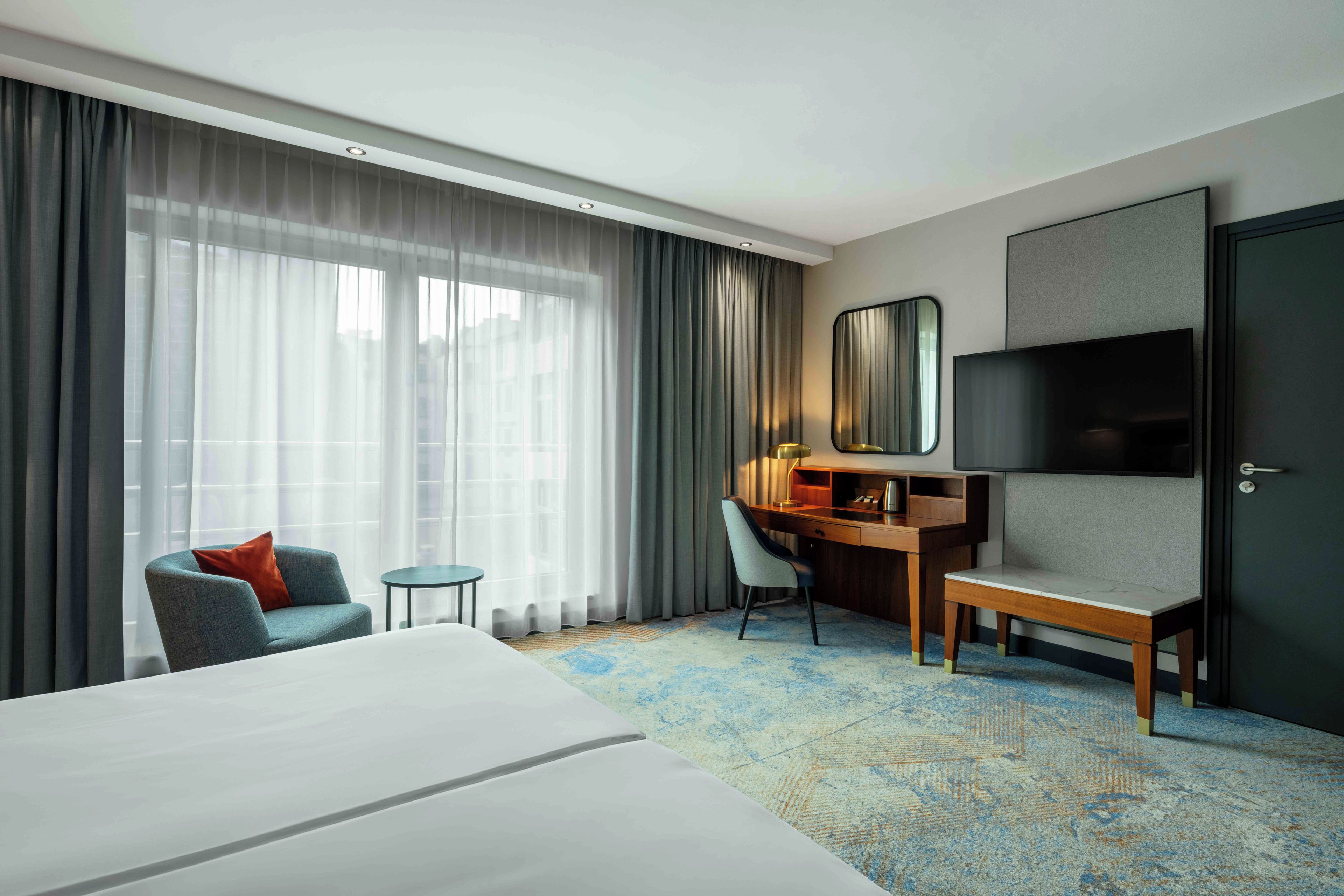 Een hotelkamer met een groot bed, een bureau met stoel, een televisie en een kledingkast.